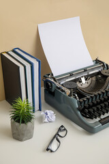 Vintage typewriter with books, houseplant and eyeglasses on table near beige wall