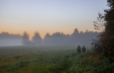Morning autumn landscape with hunters walking in the fog along the edge of the forest.