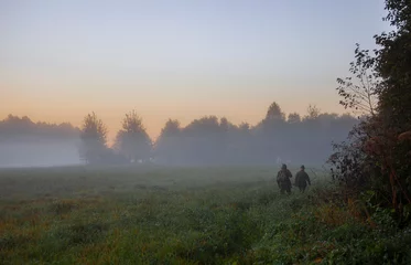 Foto op Canvas Morning autumn landscape with hunters walking in the fog along the edge of the forest. © okyela