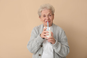 Senior woman drinking milk on beige background