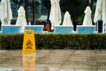 caution wet floor sign near the swimming pool during the rainy day