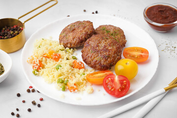 Cutlets with bulgur, boiled vegetables and tomatoes on white table in kitchen