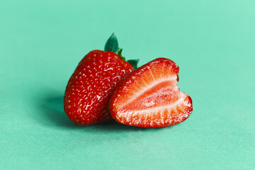 Two strawberries on a cyan background. for design with space for text. Header for design. Red ripe strawberry with leaves and half of strawberry, internal structure of strawberry