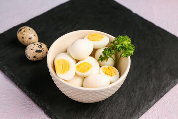 Board with bowl of boiled quail eggs on lilac background