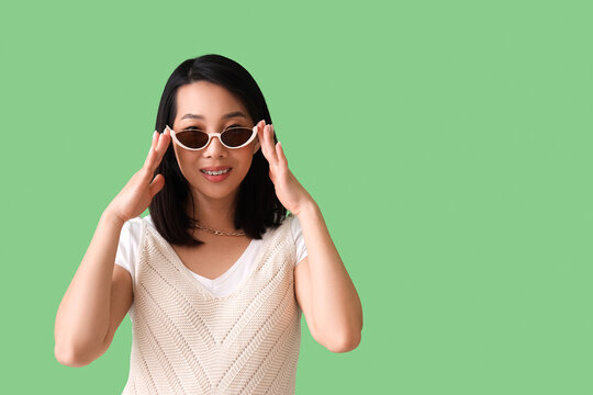 Beautiful Asian woman in stylish sunglasses on green background