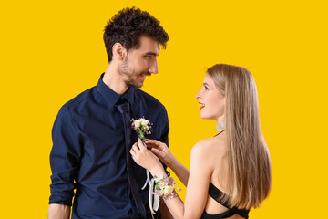 Beautiful prom couple pinning boutonniere on yellow background © Pixel-Shot