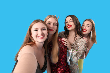 Fototapeta premium Young women dressed for prom taking selfie on blue background