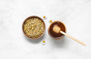 Obraz na płótnie Canvas Bowls of honey and dried chamomile flowers on light background