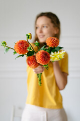 A young woman florist holds a bouquet of dahlias in front of her on a white background. Vertical image for your design, focus on flowers