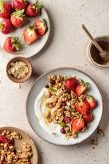 Healthy breakfast: fresh granola, muesli with yogurt, strawberry and honey on beige textured background. Top view