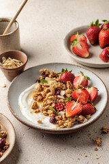 Healthy breakfast: fresh granola, muesli with yogurt, strawberry and honey on beige textured background