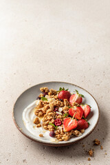 Healthy breakfast: fresh granola, muesli with yogurt, strawberry and honey on beige textured background. Copy space