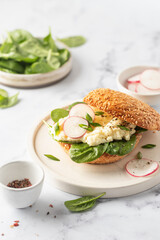 Breakfast burger with scrambled eggs, spinach, radish slices on white marble kitchen table