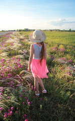 A girl in a bright dress and hat stands on a flowering field with her back, spring in the steppe, silk grass and clover
