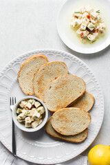 Top view of marinated feta cheese cubes and slices of toasted bread on a white plate. Cheese cubes in a ramekin with bread, flat lay of feta cheese cubes and slices of toast