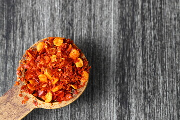Wooden bowl with crushed chili pepper and fresh red chili pepper on old table. Selective focus.