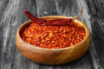 Wooden bowl with crushed chili pepper and fresh red chili pepper on old table. Selective focus.
