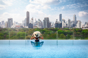 A tourist woman in a swimming pool enjoys the elevated view over the Lumphini Park and skyline of...