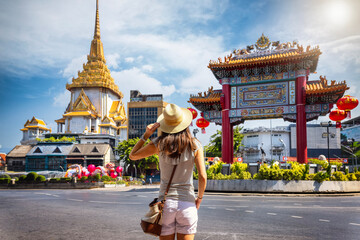 A tourist woman on sightseeing tour stands in front of the Chinatown Gate at the famous Yaowarat Road, Bangkok, Thailand