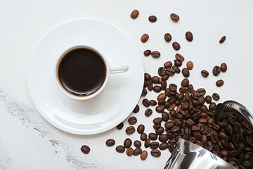 Cup of hot espresso and coffee beans on white marble background