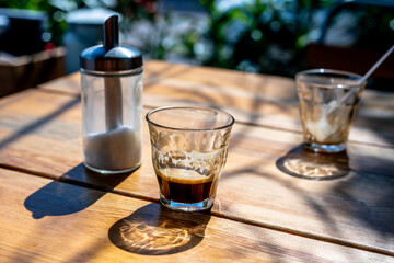 Cup of hot black coffee espresso, one empty glass and sugar on table in street cafe in sunset hours.