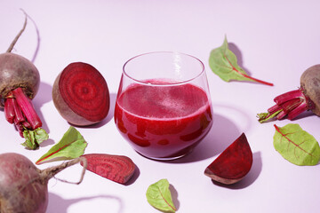 Glass of healthy beet juice and spinach on lilac background