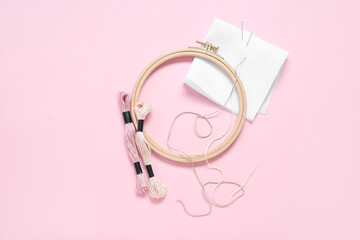 Wooden embroidery hoop with mouline threads, pins and canvas on pink background © Pixel-Shot
