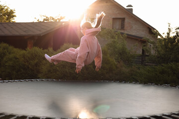 Happy little child girl having fun and jumps on trampoline outdoors, at backyard of the house on sunny summer day, active recreation on summertime vacation. Happy childhood concept. Children's day.