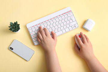 Female programmer using computer keyboard with mobile phone and earphones on beige background