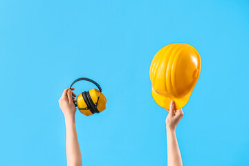 Female hands holding safety hardhat and ear muffs on blue background