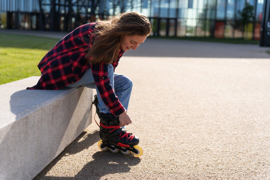 Young Pretty Woman Sitting Outdoor And Putting On Roller Blades On A Sunny Day