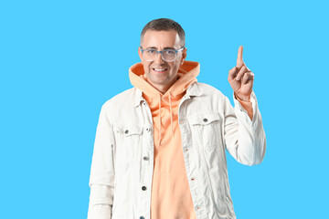 Mature man in eyeglasses pointing at something on blue background