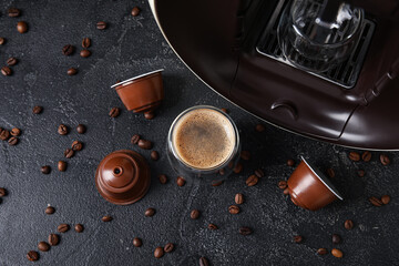 Glass of delicious espresso, capsule coffee maker, pods and beans on black grunge table