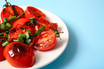 Plate with tasty grilled tomatoes and green onion on blue background