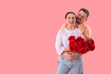 Happy engaged couple with flowers hugging on pink background