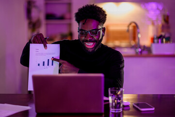 Portrait of a multicultural friendly e-commerce worker showing statistics and charts at a laptop while having an online meeting from home.