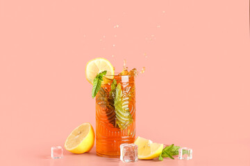 Glass of ice tea with splashes on pink background