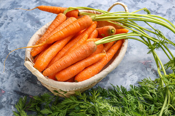 Wicker basket with fresh carrots on blue background