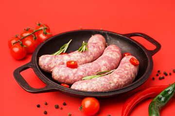 Frying pan with raw fresh sausages, tomatoes and spices on red background, closeup