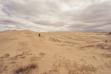 Lone man walking under the clouds across the sand at Great Sandhills Ecological Reserve