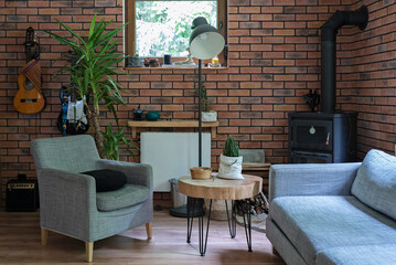 Design room in a rural cottage with comfortable sofa and armchair, red brick wall, fireplace and wooden stylish table. Cozy interior with stylish decor. 