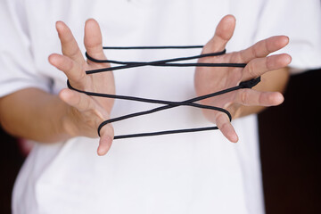 Closeup boy hands is playing rope which called cats cradle game. Concept, game involving the creation of various style figures between the fingers. Traditonal playing.       - obrazy, fototapety, plakaty