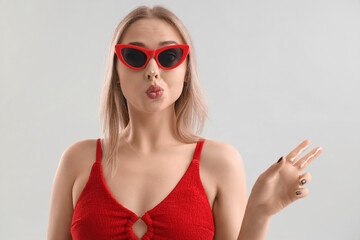 Young woman with sunscreen cream on her nose blowing kiss against light background, closeup