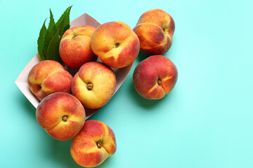 Paper plate with sweet peaches and leaves on blue background