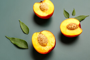 Halves of sweet peaches and leaves on green background