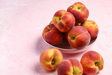 Bowl with sweet peaches on pink background