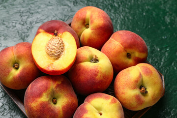 Tray with sweet peaches on green background