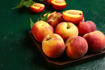 Tray with sweet peaches and leaves on green background