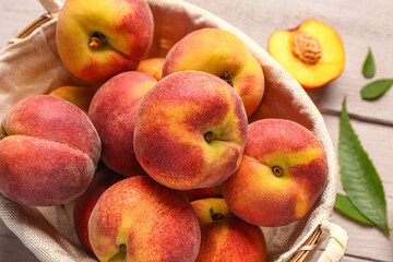 Wicker basket with sweet peaches and leaves on white wooden background