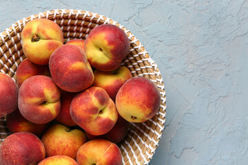 Wicker bowl with sweet peaches on blue background